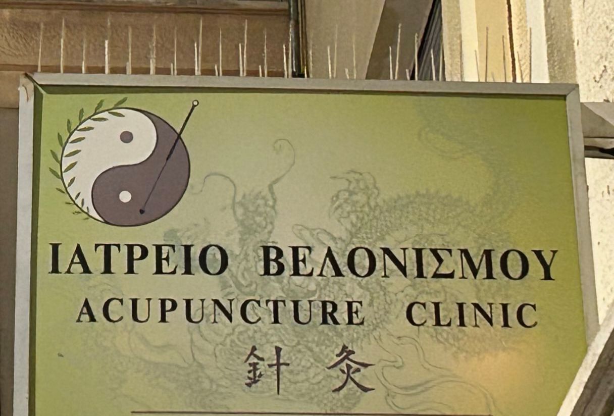 An elevated sign outside an acupuncture clinic advertising their services, with pigeon-deterrent spikes on top.